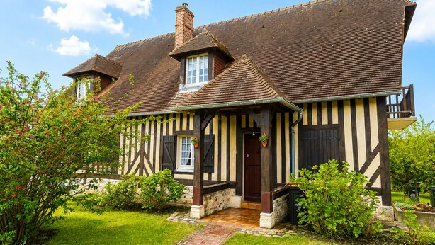 A traditional half-timbered house with a sloped roof, a brick chimney, and a stone foundation. - Under the spell (Touques)