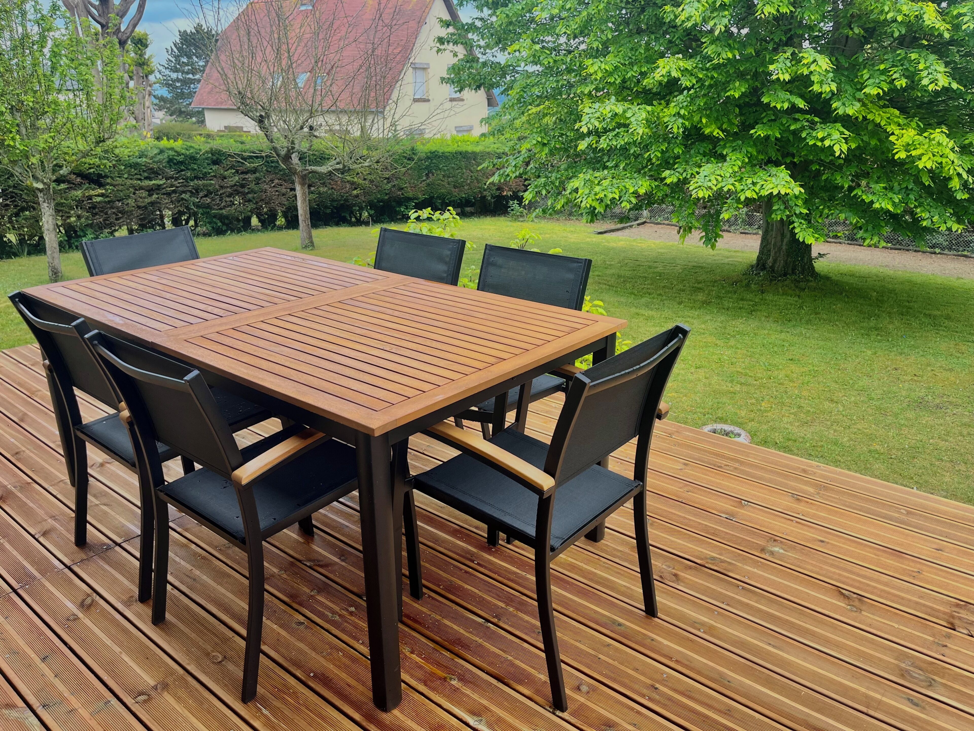 Une terrasse en bois avec une table rectangulaire et six chaises.