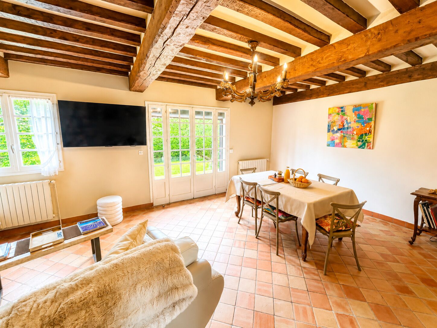 Un espace repas comprenant une table, des chaises, un lustre et une vue sur l’extérieur grâce à des portes vitrées.
