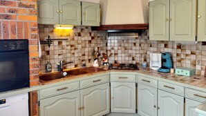 A compact kitchen with light green cabinets, a tiled backsplash, a microwave, a coffee maker, and a stove. - Under the spell (Touques)