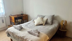 A bedroom with a bed, a desk, a chair, a lamp, and a radiator. - Under the spell (Touques)