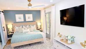 Quarto com cama, mesas de cabeceira, televisão e cômoda.