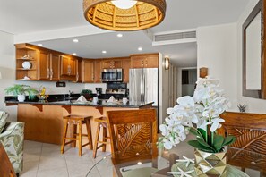 A modern kitchen with wooden cabinets, stainless steel appliances, and a central island with stools. - Ocean View 1BR Condo Near Beach, Pools & Dining -Kaanapali Shores 543 (Lahaina)