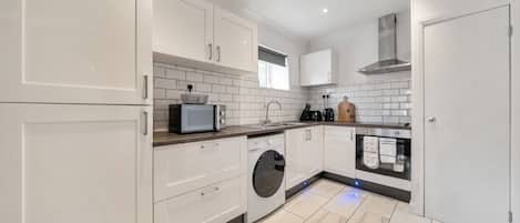 A modern kitchen with white cabinetry, a built-in washing machine, and a stainless steel range hood.