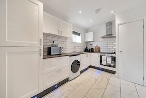 Una cocina moderna con armarios blancos, lavadora integrada y extractor de acero inoxidable.