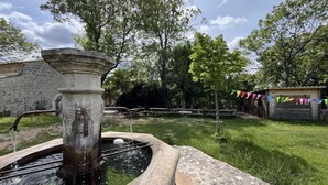 Entorno rústico al aire libre con una fuente de piedra, mesas de picnic y una estructura de madera.