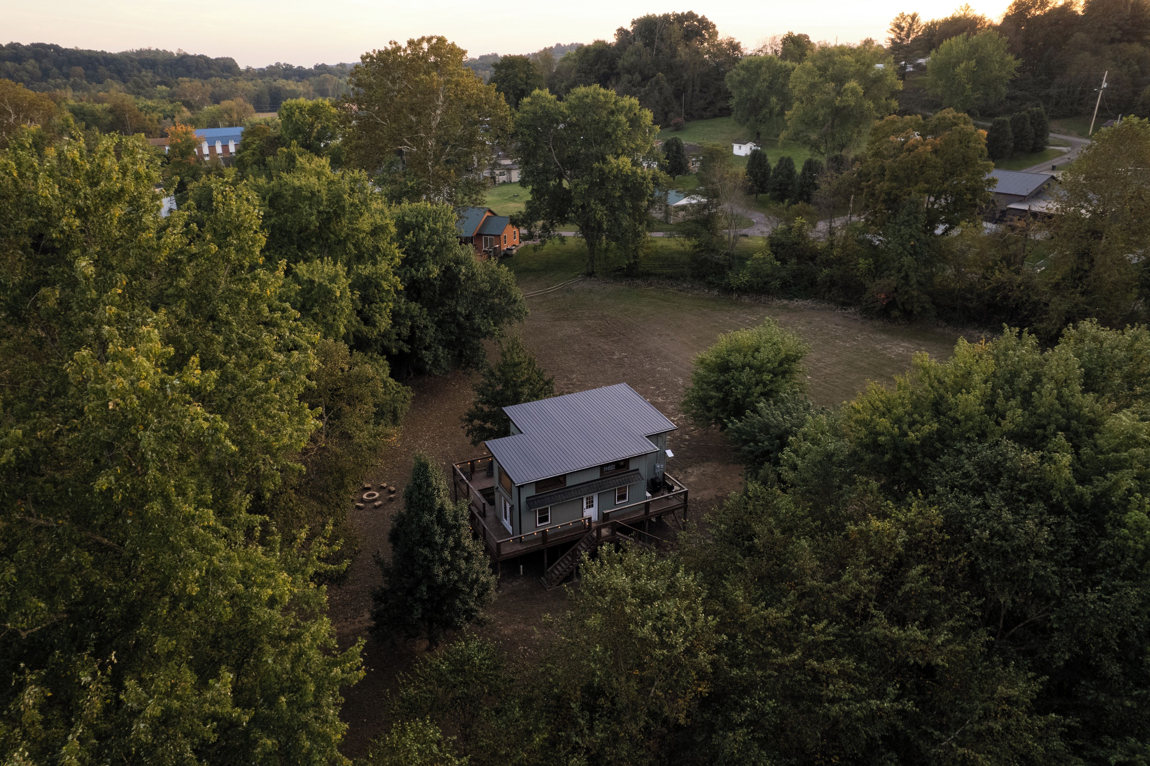 A large house with a spacious deck and a fenced yard surrounded by dense trees.