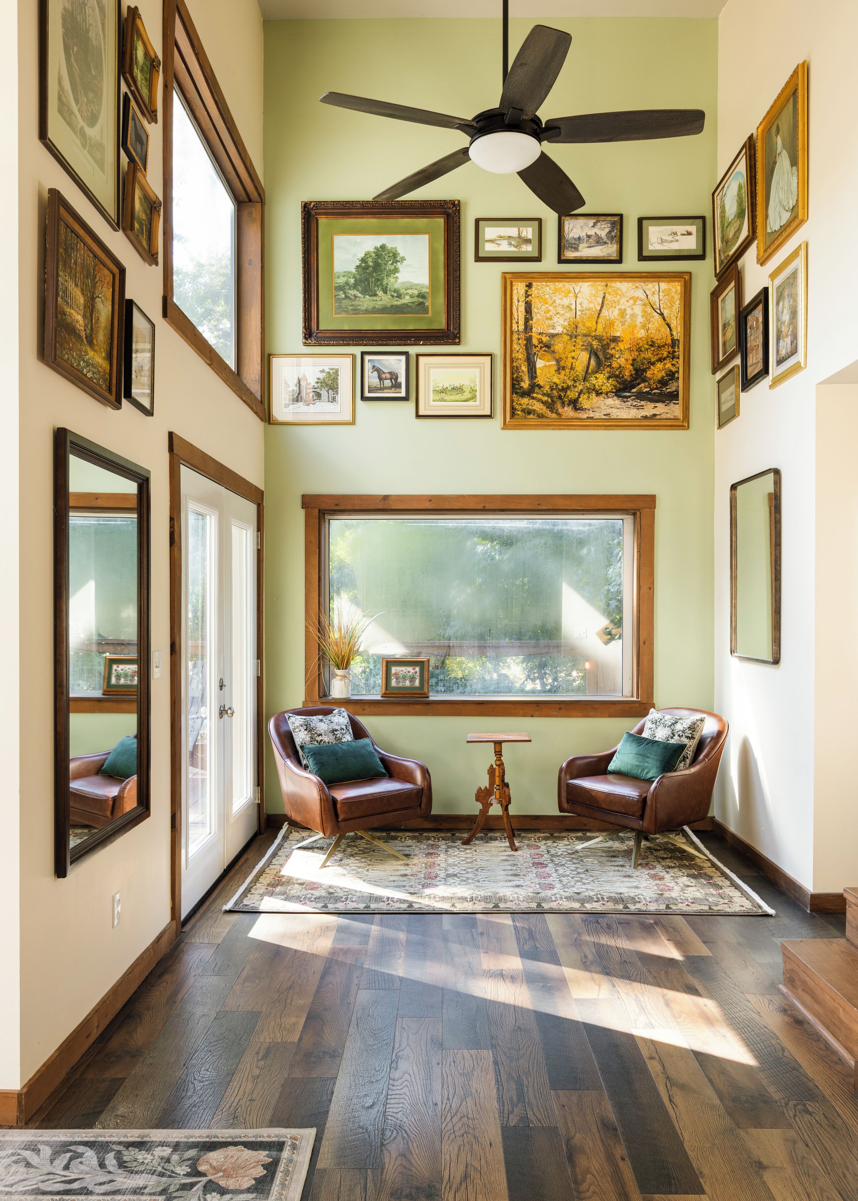 A room with hardwood flooring, two leather armchairs, a large window, and a ceiling fan.