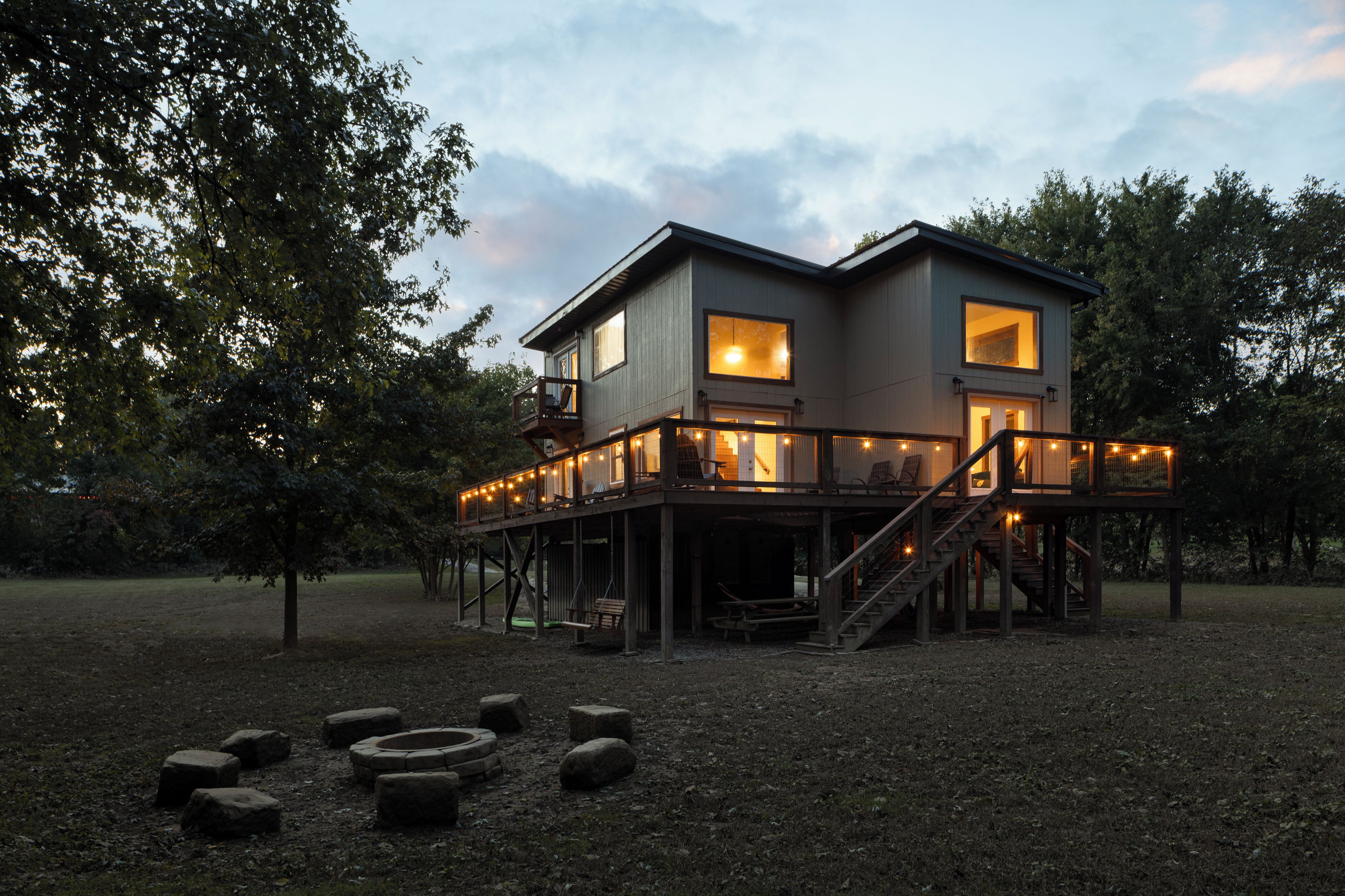 A two-story wooden house with a deck, surrounded by trees.