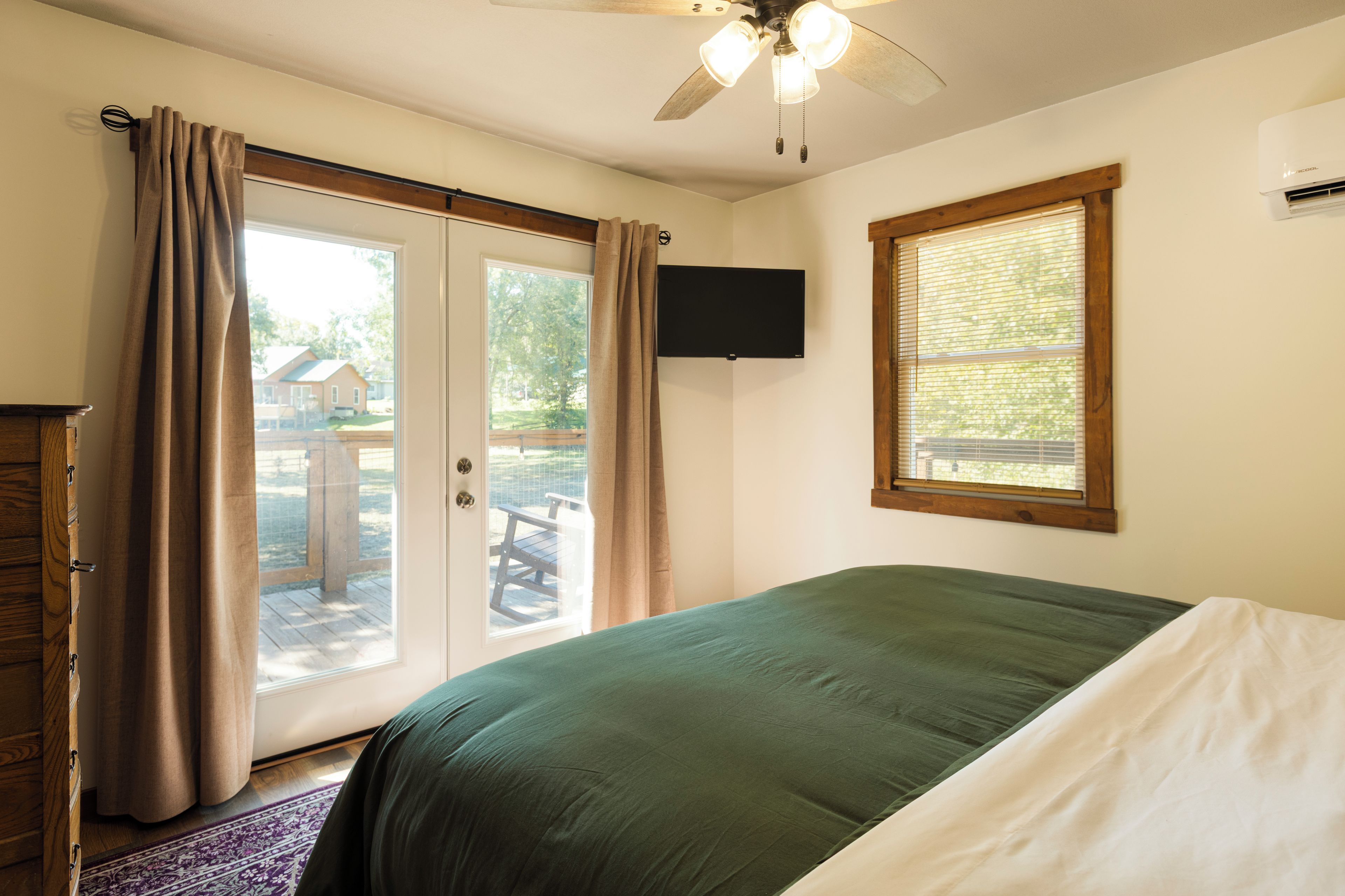 A bedroom with a bed, a ceiling fan, a TV, and a window with blinds.