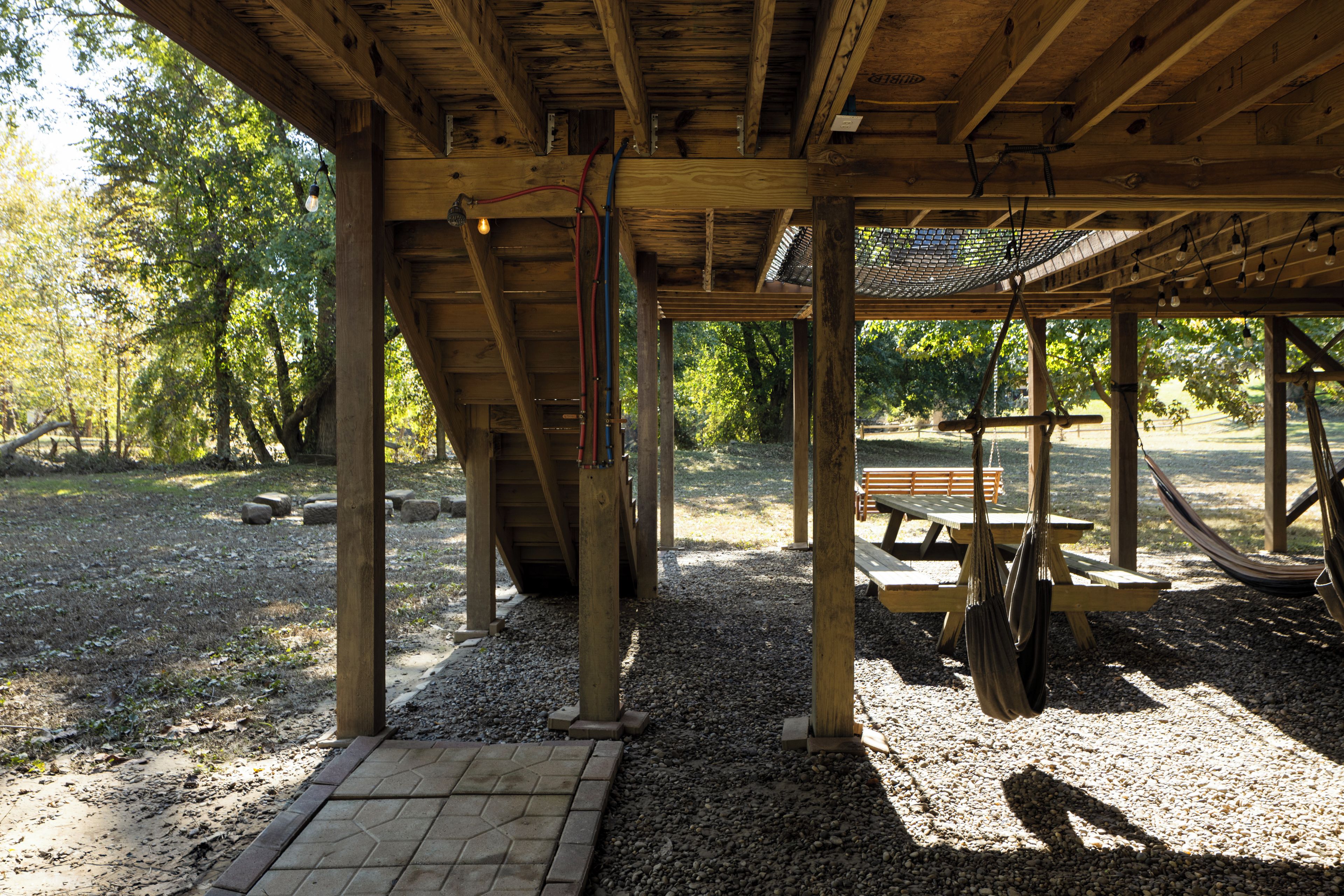 A wooden pavilion with a gravel floor, a bench, and a hammock.