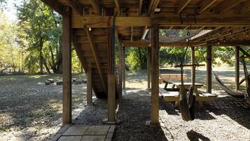 A wooden pavilion with a gravel floor, a bench, and a hammock.