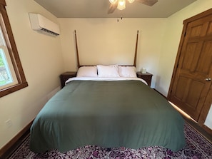 Quarto com cama de dossel, mesa de cabeceira, porta de madeira e ar condicionado na parede.