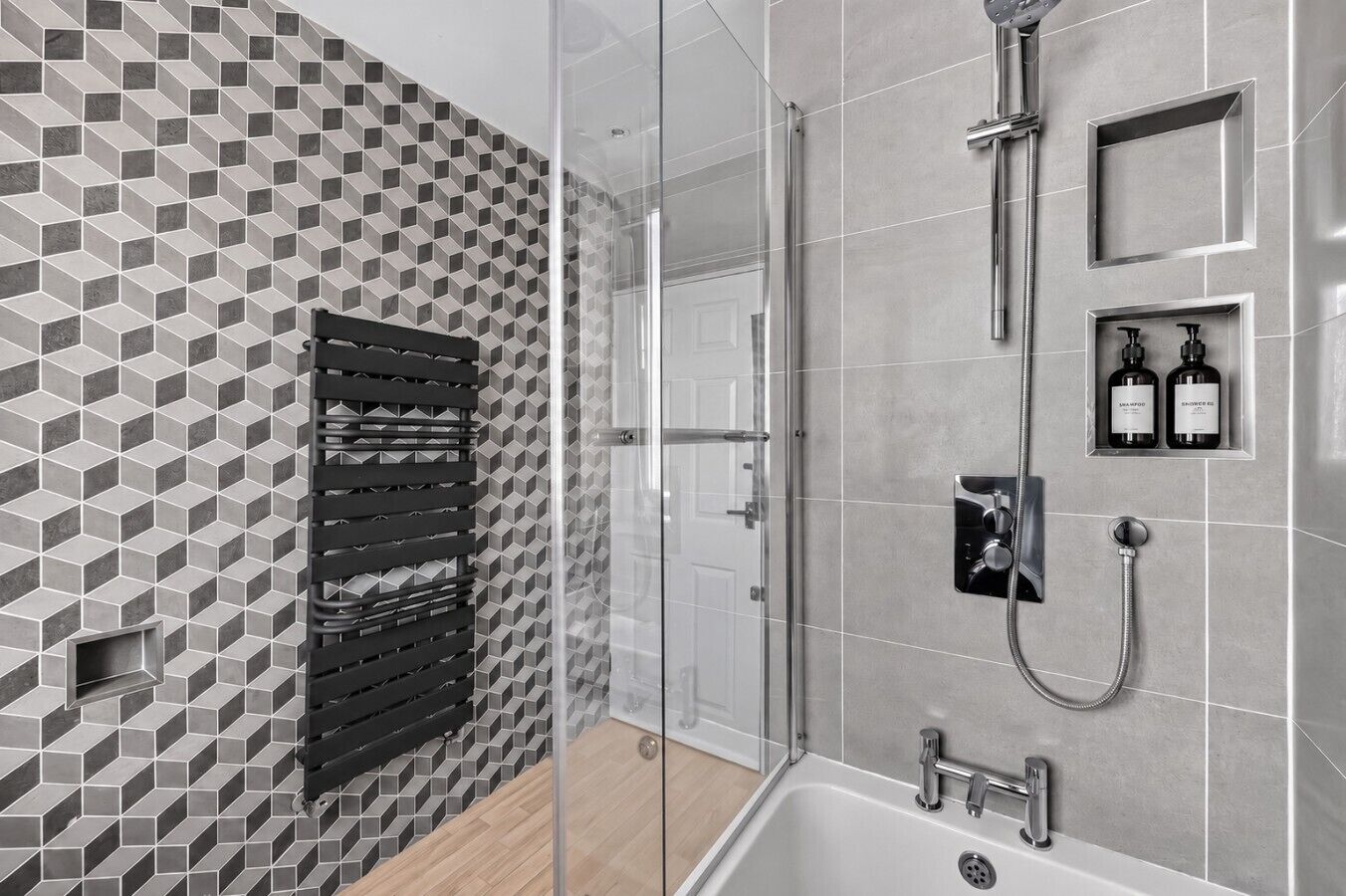Et moderne badeværelse med flisebeklædning i geometrisk mønster, en brusekabine i glas og en indbygget dispenser til shampoo og balsam.