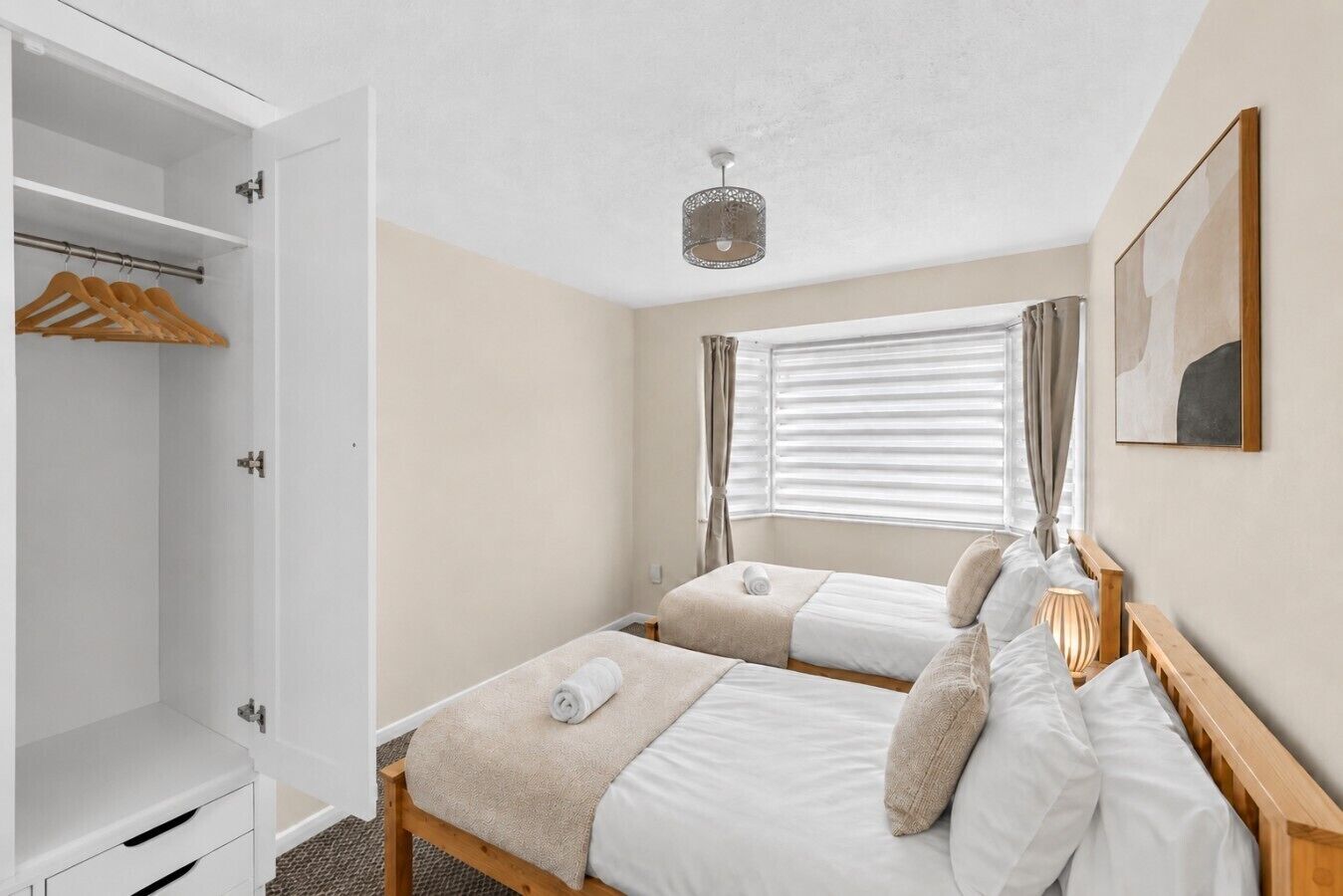 Un dormitorio con dos camas, un armario, una ventana con cortinas y una lámpara colgante.