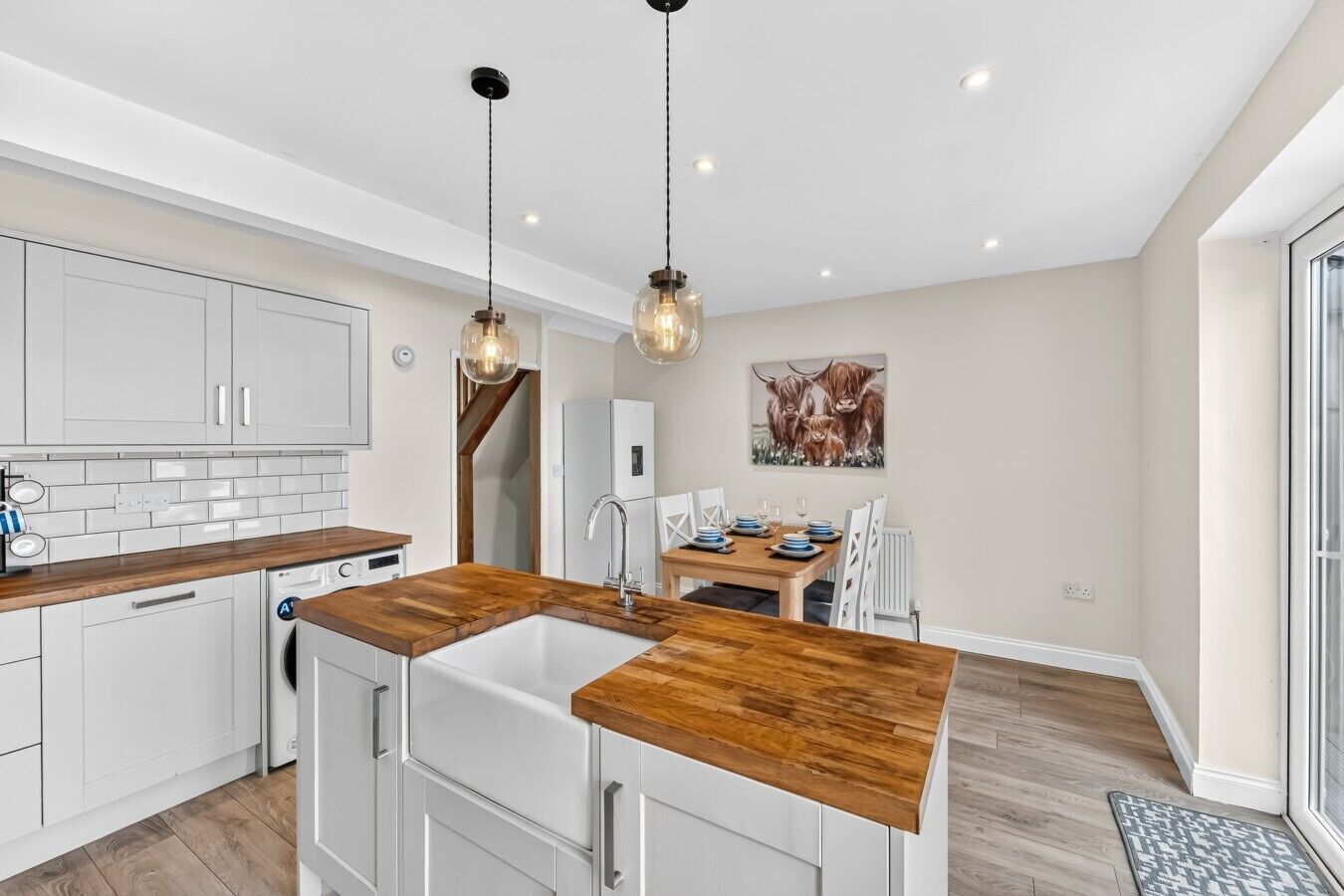 Une cuisine moderne avec des meubles blancs, des plans de travail en bois et des luminaires suspendus.