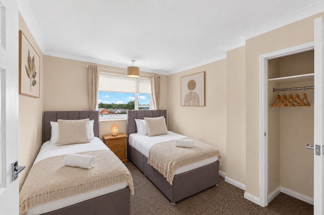 A hotel room with two beds, a window with a view, a coat rack, and a door leading to a closet.