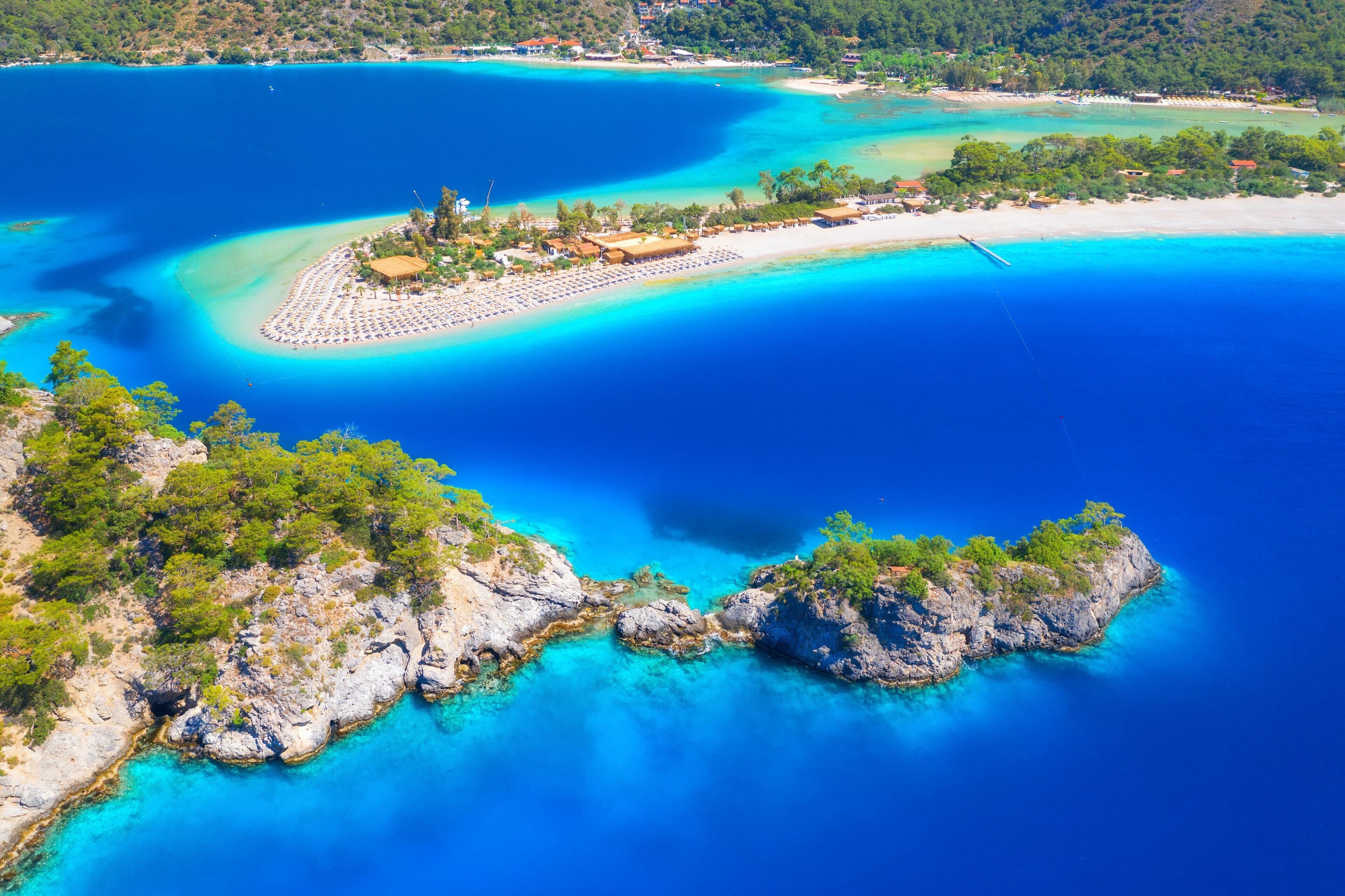 An aerial view of a coastal area with a beach, clear blue waters, and rocky terrain.