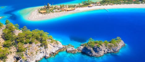 An aerial view of a coastal area with a beach, clear blue waters, and rocky terrain.