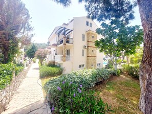 A multi-story residential building with balconies, surrounded by greenery and a paved pathway. - Mira Stay Apartment with Pool in Ölüdeniz (Ölüdeniz)
