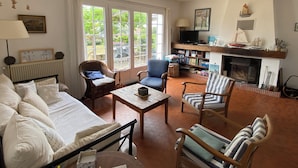 Een woonkamer met een bank, stoelen, een salontafel, een open haard en een boekenkast.