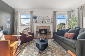 A living room with a fireplace, two sofas, a coffee table, and a view of the outdoors. - POOL , MINI GOLF & OUTDOOR MOVIE THEATER (McKinney)