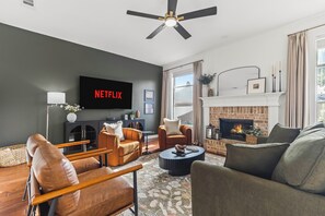 A modern living room with a fireplace, comfortable seating, a flat-screen TV, and a ceiling fan.