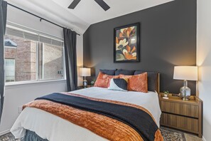 A hotel room with a bed, two bedside lamps, a framed artwork on the wall, and a window with curtains. - POOL , MINI GOLF & OUTDOOR MOVIE THEATER (McKinney)