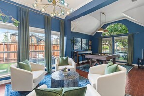 A room with a pool table, two white sofas with green cushions, a round coffee table, and a large window with curtains. - POOL , MINI GOLF & OUTDOOR MOVIE THEATER (McKinney)
