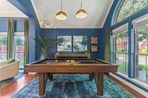 A pool table in a room with blue walls, two pendant lights, and a view of the outdoors. - POOL , MINI GOLF & OUTDOOR MOVIE THEATER (McKinney)