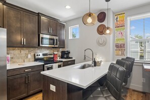 A modern kitchen with dark wood cabinets, stainless steel appliances, a white island with seating, and decorative wall art. - Y'alliday Inn - Y'all come stay in Nashville's best neighborhood. 3bed/3bath (Nashville)
