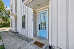 Ein Wohnhaus mit einer hellblauen Haustür, der Hausnummer '4908' an der Wand und einer Fußmatte mit dem Aufdruck 'Key Up'.
