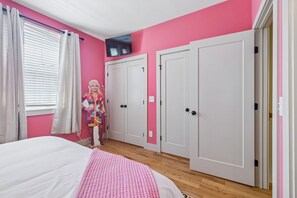 Ein Schlafzimmer mit einem Bett, einer rosafarbenen Wand, einem Fernseher und einem Kleiderschrank.
