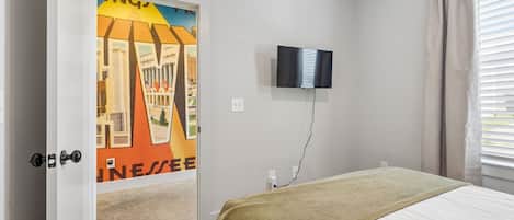 A bedroom with a bed, a television mounted on the wall, and a door with a colorful mural.