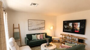 A living room with a green sofa, a white armchair, a coffee table, a TV, and a painting on the wall. - Walk to Old Town • Pool • Golf • Sleeps 10 (Scottsdale)
