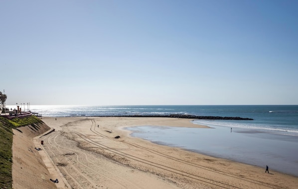 A beach with a curved shoreline, a rocky breakwater, and a clear sky. - Balcon de Santa Maria Free Parking by Cadiz Time (Provincia de Cádiz)