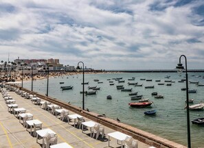 A coastal area with a promenade lined with tables and chairs, boats on the water, and buildings in the background. - Balcon de Santa Maria Free Parking by Cadiz Time (Provincia de Cádiz)