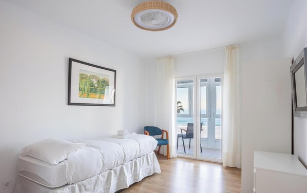 A bedroom with a bed, a chair, a window with a view of the beach, and a ceiling fan. - Balcon de Santa Maria Free Parking by Cadiz Time (Provincia de Cádiz)