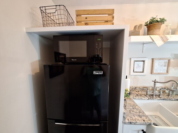 Una cocina con un refrigerador negro, un microondas y un flete de madera encima.
