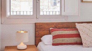 A bedroom with a wooden headboard, a white lamp on a bedside table, and a window with a view of buildings. - New penthouse with a private terrace in the heart of Cádiz. (Ciudad de Cadiz)
