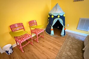 Una habitación con una pared amarilla, una tienda de juegos, dos sillas y una alfombra pequeña.