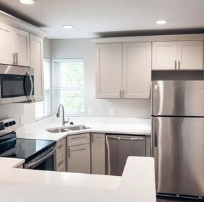 A modern kitchen with stainless steel appliances, white cabinetry, and a window providing natural light. - 1 B/1 BA fully furnished unit in luxury apartment community/ Indianapolis/ 46260 (Indianapolis)
