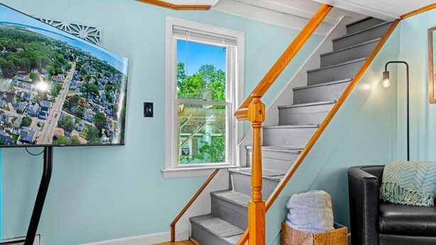 Una escalera con barandillas de madera, un televisor montado en la pared y vistas a una zona residencial a través de una ventana.