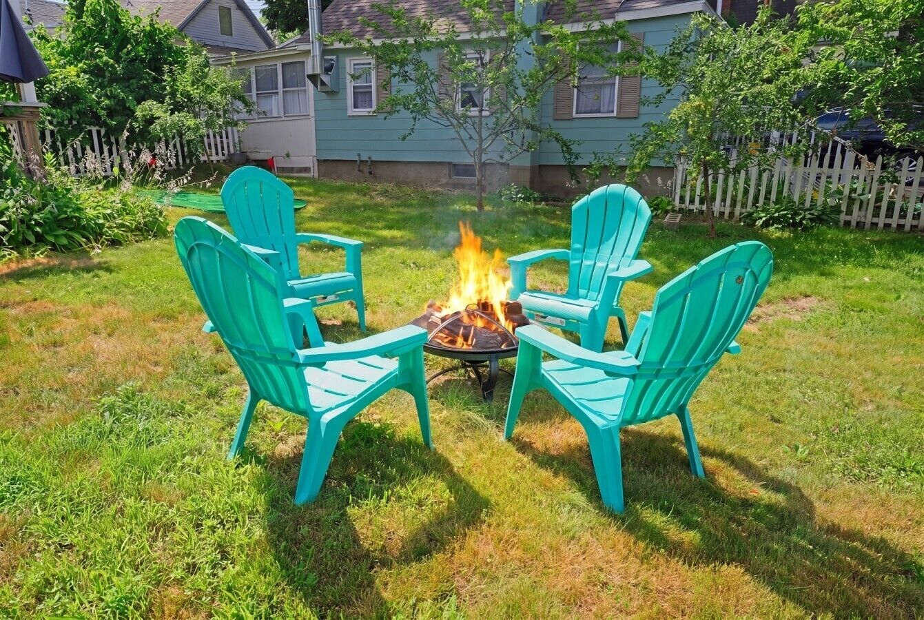 A fire pit with four chairs arranged around it in a backyard.
