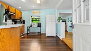 Cocina con armarios de madera, refrigerador blanco, microondas y ventana con vista a follaje.