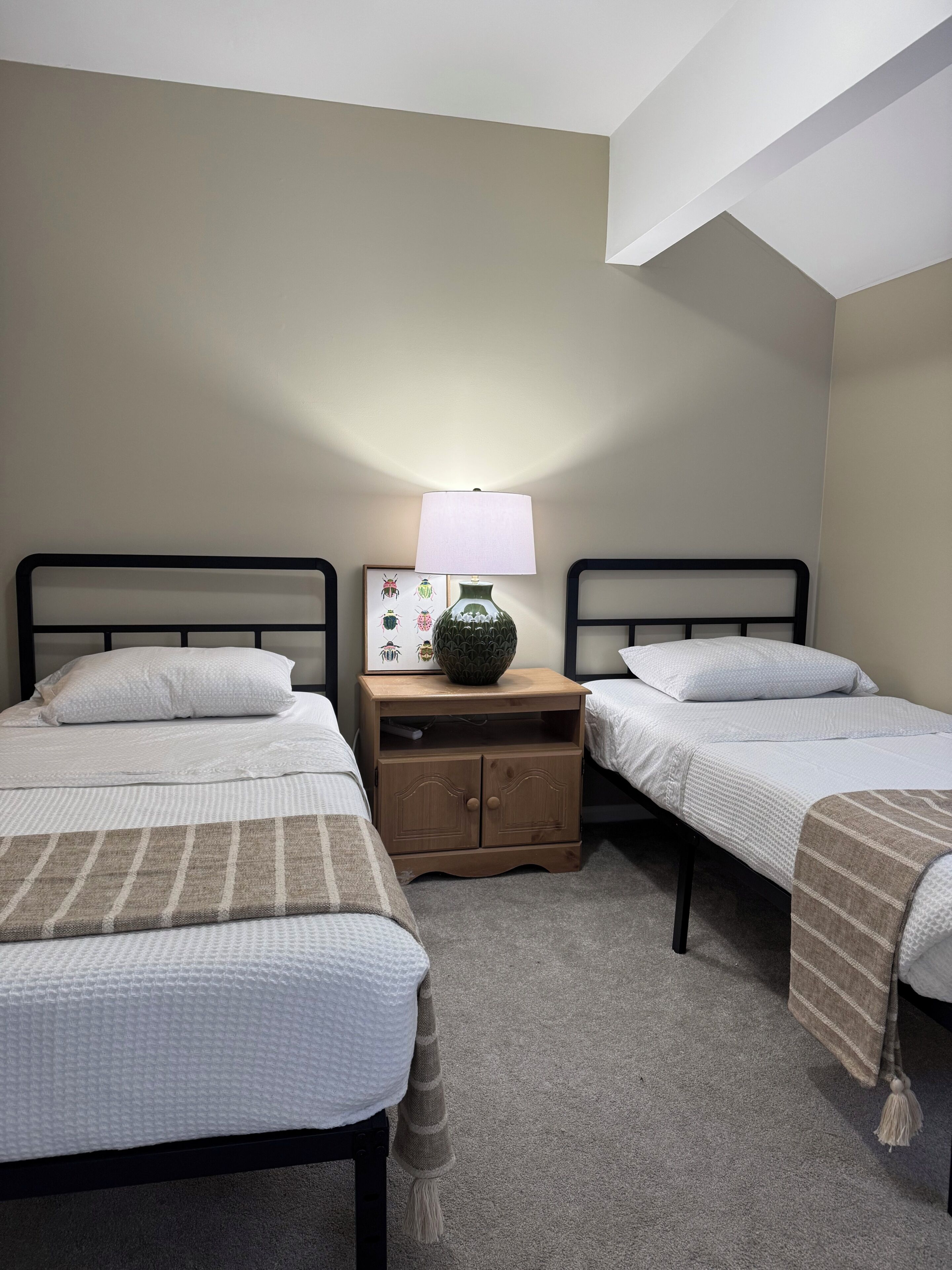 A bedroom with two beds, a nightstand with a lamp, and a framed picture on the wall.