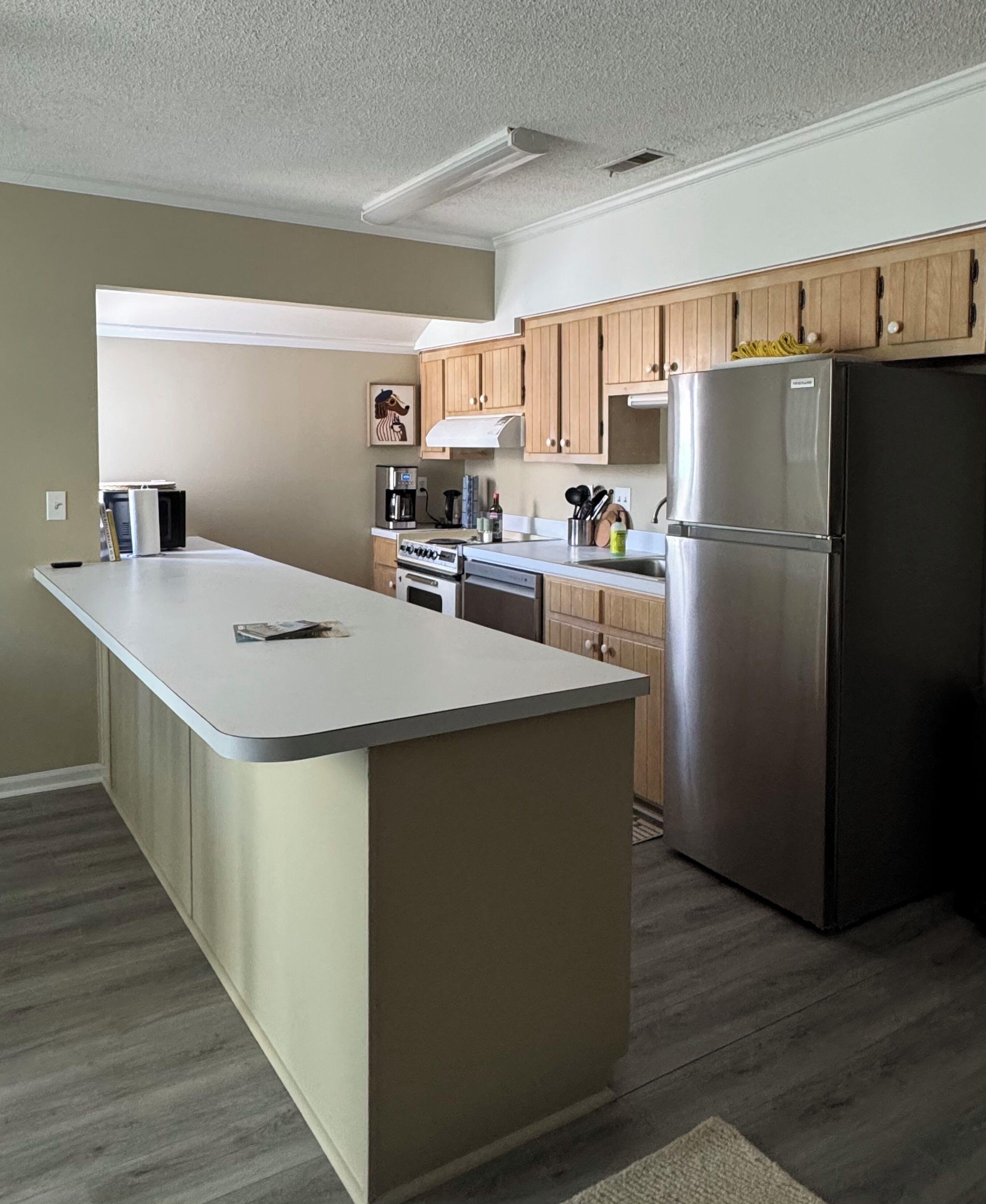 A modern kitchen with a central island, stainless steel appliances, wooden cabinets, and a view to the living area.