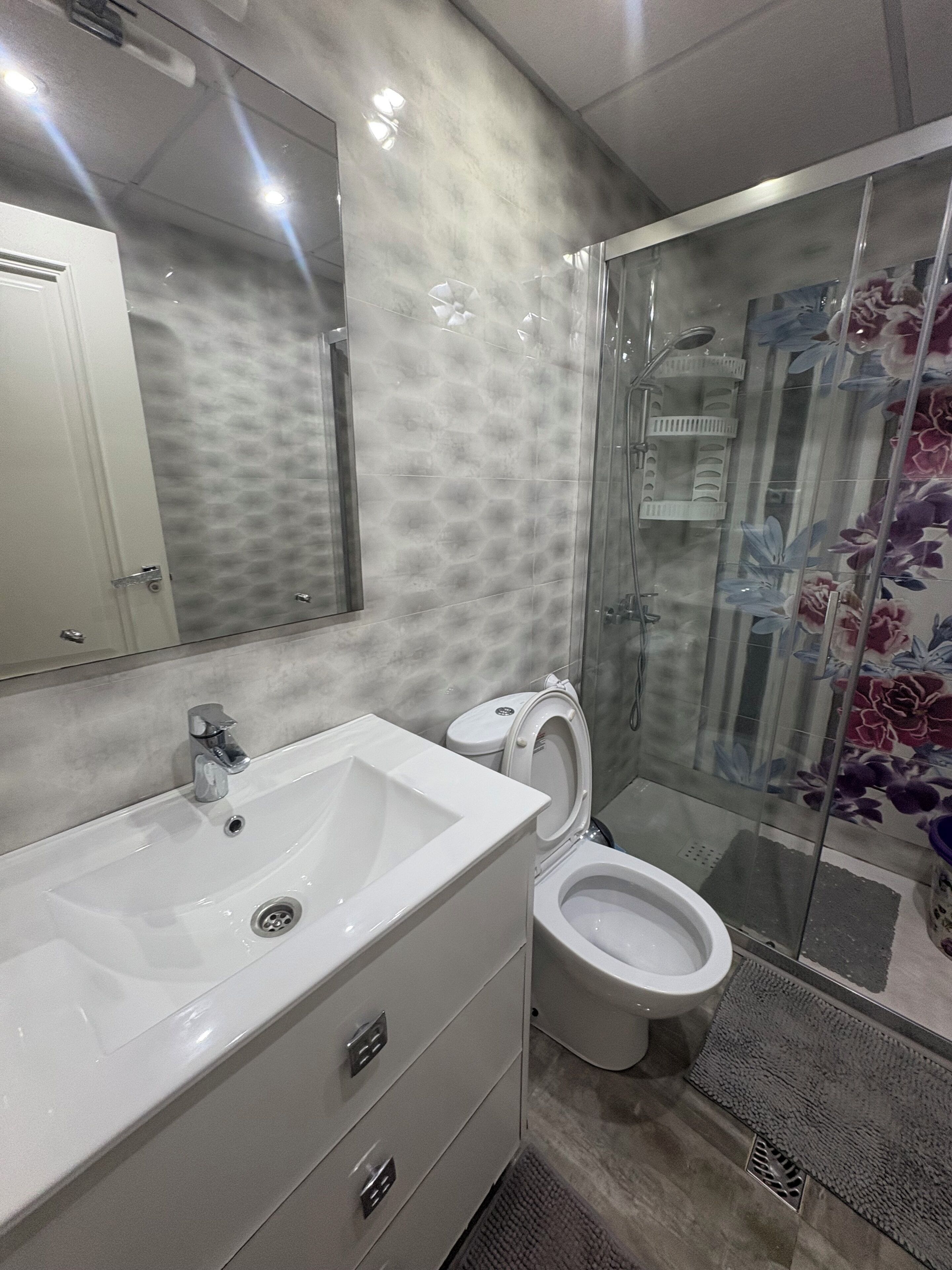 Un bagno con lavandino, specchio, servizi igienici e doccia, tutti in bianco.