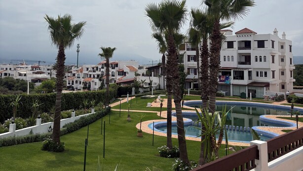 Een resort met een zwembad, palmbomen en witte gebouwen.
