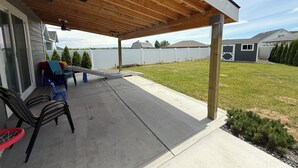 Ein überdachter Patio-Bereich mit Deckenventilator, Gartenmöbeln und einem Basketballkorb.
